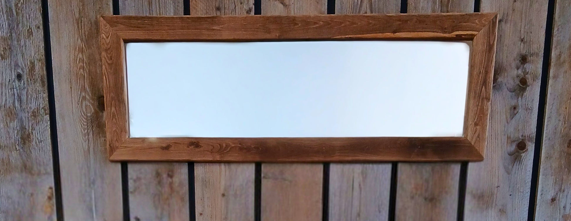 Rustic reclaimed wood 'Boëme' mirror made from solid oak, staged against a black accent wall with vertical scaffolding planks. 