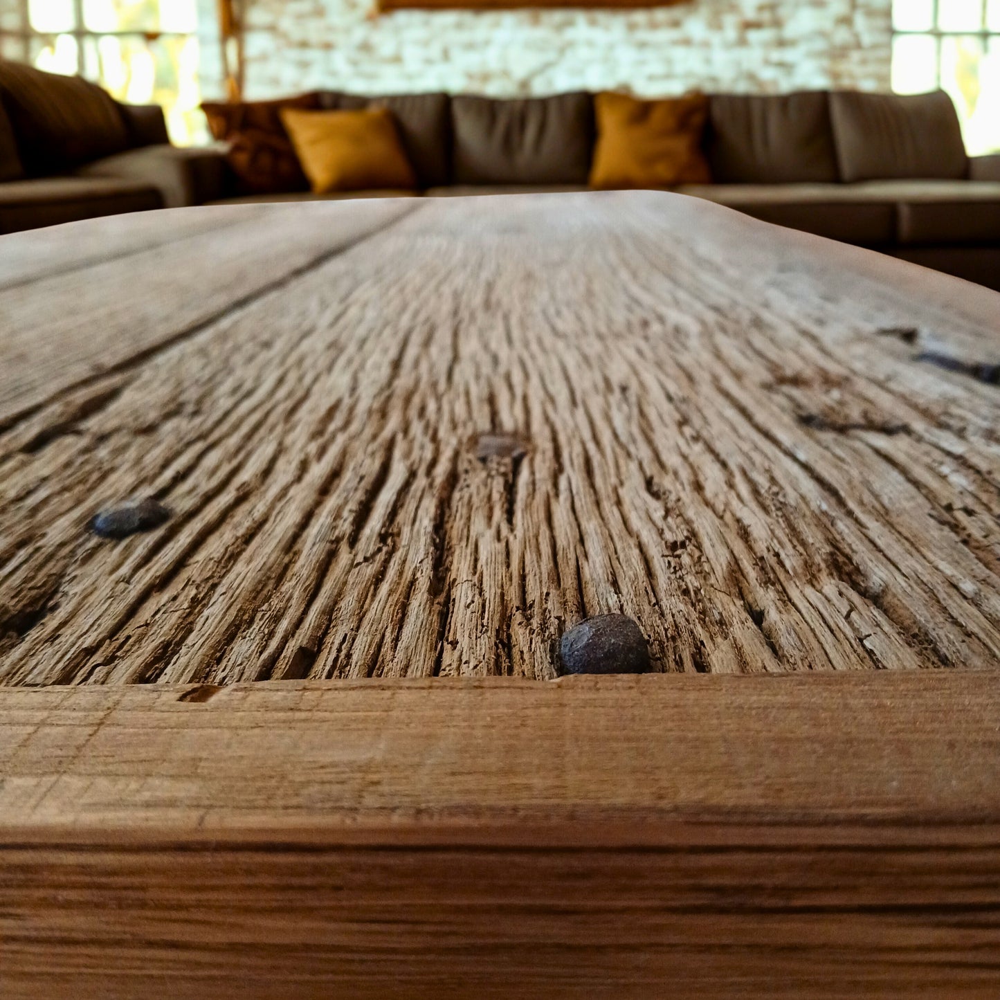 Close-up of handcrafted solid French Oak coffee table using reclaimed wood and recycled materials, set in a New York Loft style living room with large, modern panoramic sofa set.