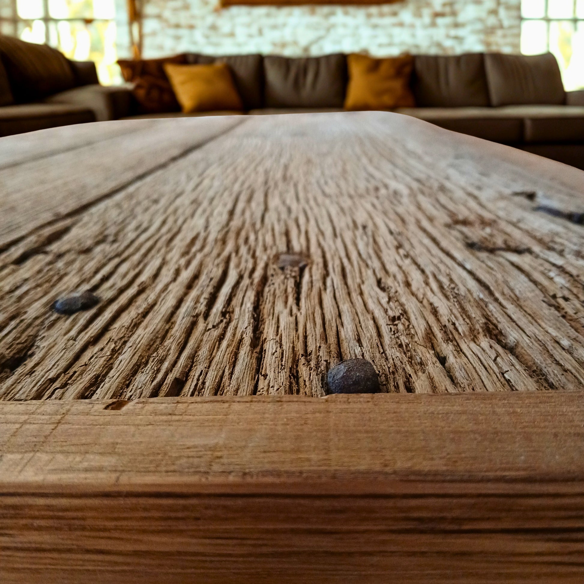 Close-up of handcrafted solid French Oak coffee table using reclaimed wood and recycled materials, set in a New York Loft style living room with large, modern panoramic sofa set.