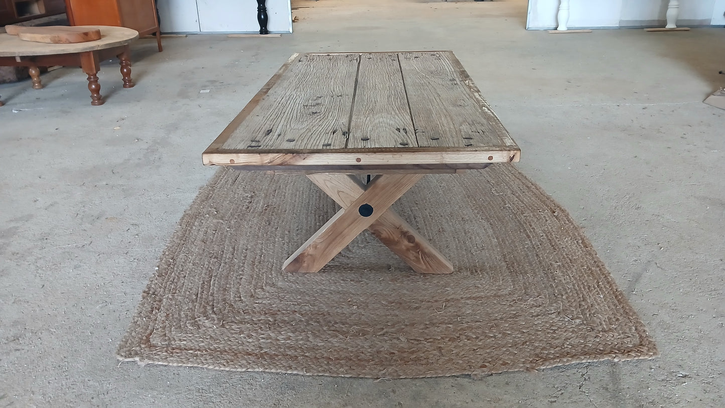 Full-length view of the Lisonne reclaimed French oak coffee table, showing rugged old oak door surface with original nail heads and complete X-shaped farmhouse legs, handcrafted in France.
