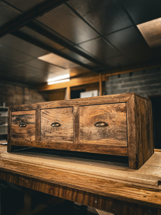 Side angle view of the mango wood sideboard or media unit from the Relooking collection, showing drawers with reclaimed brass half-moon handles, highlighting the satin finish and compact design.